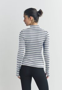 Dolga majica z navpičnimi belimi in mornarsko modrimi črtami, z rebrasto teksturo in oprijetim krojem, kombinirana s črnimi pajkicami.