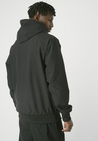 Schwarze Kapuzenjacke mit glatter Textur, elastischen Bündchen und Saum. Sie hat eine lockere Passform mit minimalistischem Design und ohne sichtbare Logos.