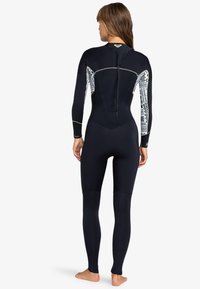 Traje de neopreno negro con mangas estampadas, mangas largas, piernas de longitud completa, cremallera trasera y costuras y acentos de logo en amarillo contrastante.