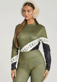 Elastisk, olivengrøn skijakke med lange sorte ærmer og et hvidt logobånd. Parret med matchende højtaljede leggings. Bløde ørevarmere i kunstpels.