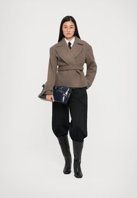 Brown belted wrap jacket, black wide-leg trousers, black knee-high boots, and a navy handbag. Smooth fabric with structured design.