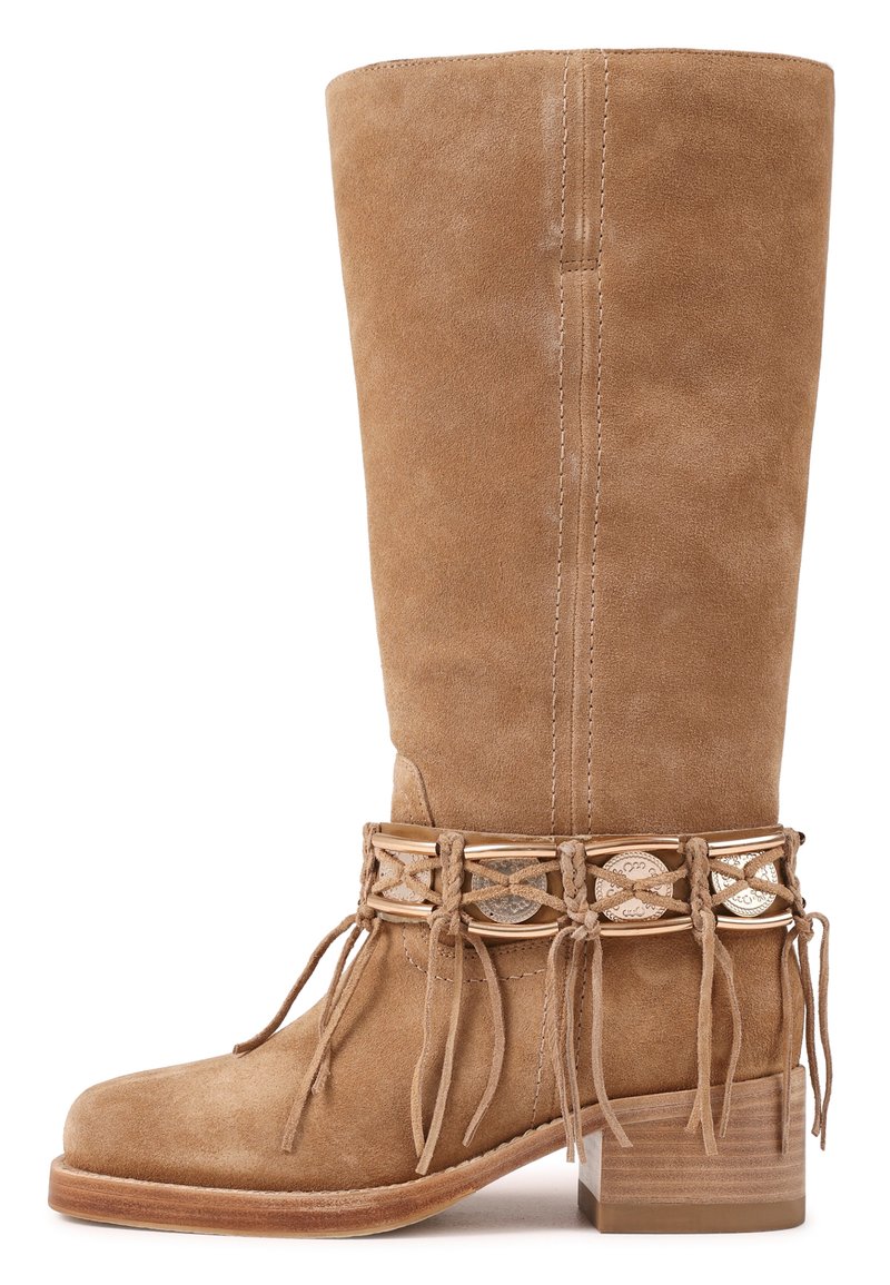 Botte haute en daim beige avec un talon bas empilé, sangle tressée décorative avec conchos métalliques et franges autour de la cheville.
