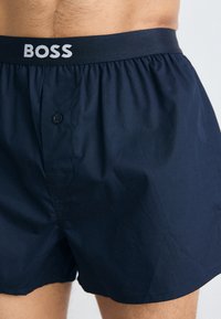 Mornarske bokserice iz lahkega blaga, z elastiko na pasu, ki nosi logotip "BOSS", sprednjim gumbom in gladko teksturo.