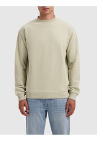 Lichtgroene sweatshirt met ronde hals, ribgebreide manchetten en onderkant, gemaakt van zachte stof. Draagt een lichtblauwe spijkerbroek. Eenvoudig ontwerp, geen patronen.