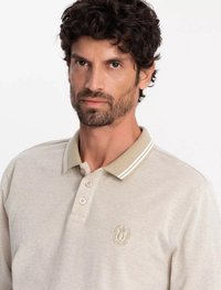 Beige polo tričko s texturovaným povrchem, s béžovým límcem a bílými pruhy a výšivkou loga na levé části hrudi.