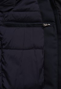 Navy sinica takki sisäpuoli, jossa on tikatut osiot, ja siinä on vetoketjullinen tasku sekä sileä kangasreunus.