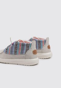 Zapatos de lona gris con tejido estampado colorido, punta redonda y suela de goma blanca. Presentan un parche de marca en tono marrón en el talón.