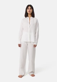 Set di camicia e pantaloni in lino bianco, caratterizzato da una chiusura a bottoni sul davanti, maniche lunghe e pantaloni a gamba larga con una consistenza liscia.