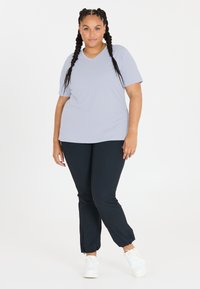 Lys grå t-shirt med V-hals parret med sorte bukser med elastiske manchetter og hvide sneakers. Glat stof med en afslappet pasform.