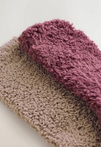 Textilierter Teppich in zwei Farben: Tiefpurpur oben, weiches Beige darunter. Er besitzt eine plüschige, samtige Oberfläche mit ungleichmäßiger Florhöhe.