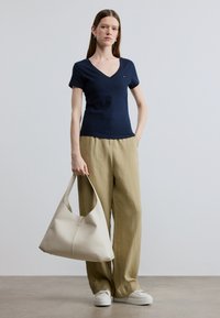 Μπλε σκούρο μπλουζάκι V με κοντά μανίκια, σε συνδυασμό με ανοιχτό μπεζ λινό παντελόνι και μεγάλη κρέμα τσάντα hobo, φορεμένο με λευκά αθλητικά παπούτσια.