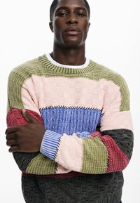 Multi-colored knit sweater featuring blocks of textured pink, green, blue, red, and black, with a ribbed neckline and cuffs.