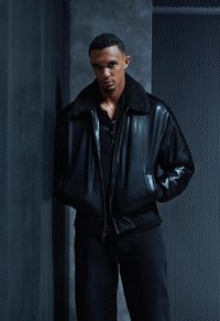 Mustast nahast pommitaja-jope karvase kraega, lukuga kinni, küljetaskutega, kantud musta nööpidega särgi ja tumedate pükstega.