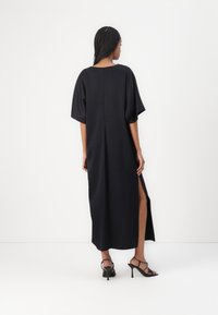 Svart maksimalkjole med korte, vide ermer, sidesplit og lukkning bak med glidelås. Glatt stoff med minimalistisk design.
