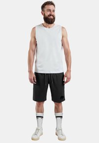 Witte mouwloze tanktop, zwarte shorts met een berenlogo, witte sokken met zwarte strepen en witte sneakers. Casual sportkleding.