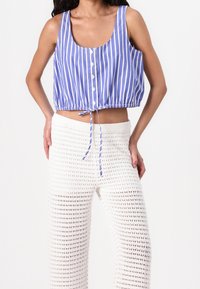 Modrý a bílý pruhovaný bezramínkový crop top s knoflíky a stahovací spodní částí, doplněný bílými volnými kalhotami s otevřeným pletením.