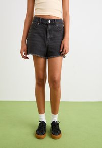 Zwarte denim shorts met een rafelrand, hoge taille, vijf zakken, gecombineerd met zwarte sneakers en witte crew socks. Eenvoudig, casual ontwerp.