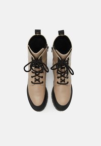 Bottes en cuir beige avec semelles en caoutchouc noir, dotées de lacets noirs, de fermetures éclair et d'une finition lisse et texturée.