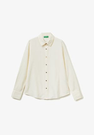 Camicia crema a maniche lunghe con collo appuntito e bottoni dorati, distesa su sfondo bianco.