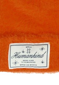 Tessuto arancione soffice con un'etichetta bianca. L'etichetta presenta testo nero, stelle e un bordo, con le scritte "Umanità" e "Fatto sulla Terra."