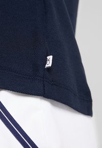 Navy blue polo shirt with textured fabric, small side logo tag, and white accents on the hem, showcasing a structured design.