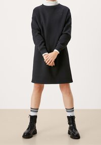 Vestido sudadera negro de corte relajado, con puños acanalados y escote redondo, acompañado de calcetines blancos hasta la rodilla con rayas negras y botas de combate.