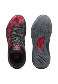 Des chaussures de sport noires et rouges présentent un dessus en camouflage texturé, un système de laçage et une semelle en caoutchouc gris à motifs avec une accent rouge.