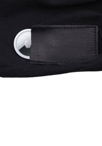 Apple AirTag blanc partiellement inséré dans une poche en cuir noir sur un tissu noir.