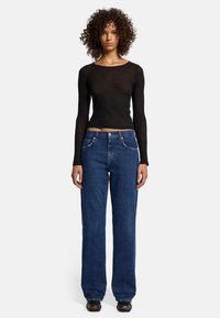 Top nero a maniche lunghe con un design aderente, abbinato a jeans dritti in denim blu a vita alta e scarpe nere, vista frontale.