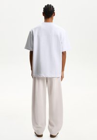 White cotton t-shirt with a relaxed fit and short sleeves, paired with light beige wide-leg trousers. Simple design, no visible patterns.