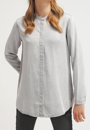 Camicia grigia chiaro con bottone, orlo arrotondato, maniche lunghe e una texture sottile. Presenta un colletto e un design del davanti semplice.