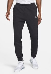 Schwarze Fleece-Trainingshose mit elastischem Bund, Bündchen an den Knöcheln und einem weißen Nike-Logo am linken Oberschenkel. Weicher Stoff, bequeme Passform.