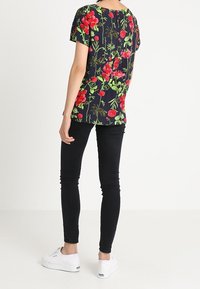 Marineblaues Floral-T-Shirt mit roten und grünen Blumen; kurze Ärmel, lockere Passform. Kombiniert mit schwarzen Skinny Jeans und weißen Sneakers.