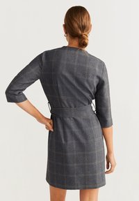 Vestido gris a cuadros con mangas tres cuartos y un cinturón. Hecho de una tela con una textura sutil, presenta un corte ajustado y llega a la rodilla.
