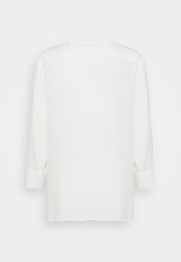 Camicia bianca a maniche lunghe con orlo dritto, mostrata da dietro su uno sfondo bianco semplice.