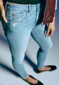 Ljusblå denimjeans har ett slitet mönster och en klassisk femfickdesign. Slät struktur med en kroppsnära silhuett.