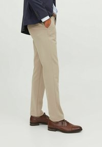 Beżowe, dopasowane spodnie wykonane z gładkiego materiału, o prostych nogawkach i bocznych kieszeniach, zestawione z brązowymi skórzanymi sznurowanymi butami.