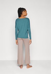 Langærmet teal top med vid halsudskæring, parret med lyse beige flared bukser med sideslidser i kanten.