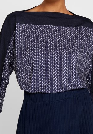 Top de manga larga azul marino con patrón de media luna blanco en el frente y mangas lisas azul marino, combinado con una falda azul marino acanalada.