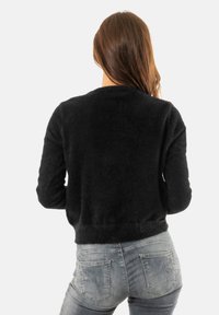 Maglione nero e morbido con scollo rotondo e maniche lunghe, abbinato a jeans grigi chiari aderenti con tasche posteriori e cuciture sottili.