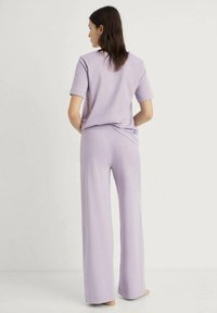Fialový dvoudílný outfit vyrobený z měkké látky, obsahující top s krátkými rukávy a kalhoty s širokými nohavicemi a elastickým pasem. Jednoduchý design.