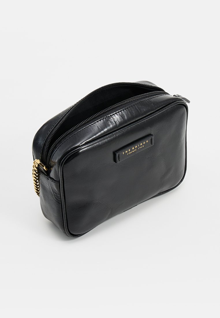 Borsa rettangolare in pelle nera con una finitura liscia, chiusura con zip superiore e hardware color oro. Presenta una placca con logo sul davanti.