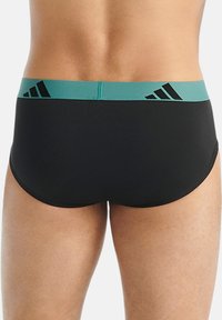 Svarta sim-kalsonger med en turkos midjeband, prydda med ett upprepande svart Adidas-logotyp och slät yta. Bakifrån visas en kroppsnära passform.