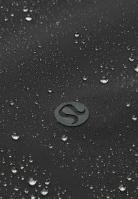 Zwart waterafstotend stof met waterdruppels. Bevat een subtiele logo in de hoek, een gladde textuur en een consistente matte afwerking.