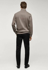 Sweatshirt gris avec col montant, texture douce, associé à un pantalon noir et des chaussures noires. La vue montre l'arrière de la tenue.