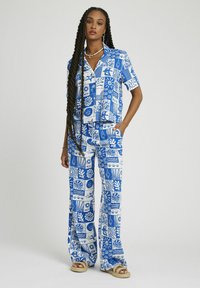 Ensemble coordonné bleu et blanc avec une chemise à manches courtes et un pantalon large, ornés de divers motifs inspirés de la nature. Tissu texturé.