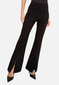 Černé rozšířené kalhoty se bočními rozparky, vyrobené z elastické tkaniny. Mají vysoký pas a plochý přední design. Kombinováno s černými špičatými podpatky.