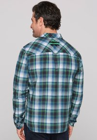 Camicia a maniche lunghe da uomo in plaid con un motivo a quadri verde, blu navy e bianco, dotata di colletto e polsini con bottone. Dettaglio del logo sul giromanica posteriore.