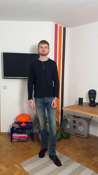 Svart långärmad tröja med henleystickning, ljusblå jeans och bruna läderskor. Mot en minimalistisk interiör.