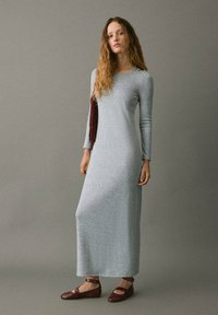 Lungo vestito in maglia grigia con maniche lunghe, scollo a giro e fenditure laterali, abbinato a scarpe basse bordeaux con dettagli a strap.
